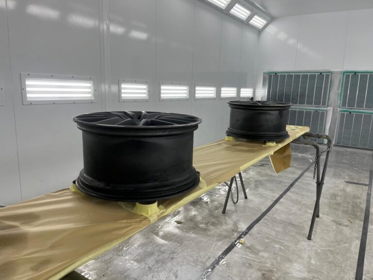 Twee zwarte velgen in spuitcabine voor autolak.