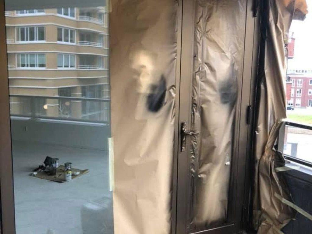 Afgeplakte ramen op balkon met appartementgebouw op achtergrond.