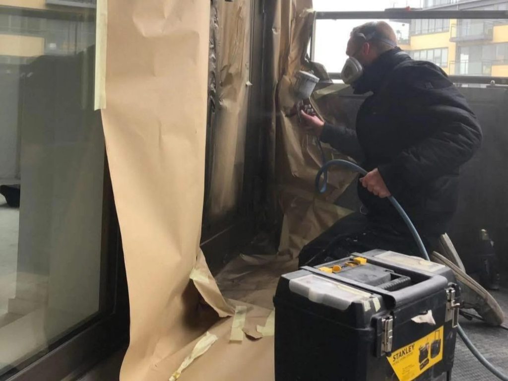 Man spuit lak op afgescherpte ramen in werkplaats.