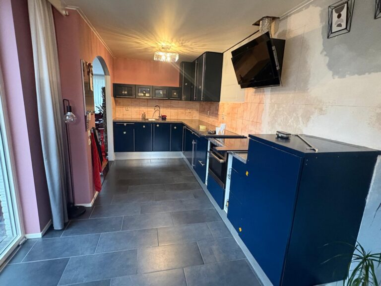 Moderne keuken met blauwe kasten en beige tegels.