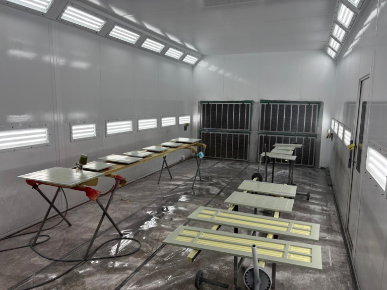 Schilderij in spuitcabine met droogrekken en ventilatie.