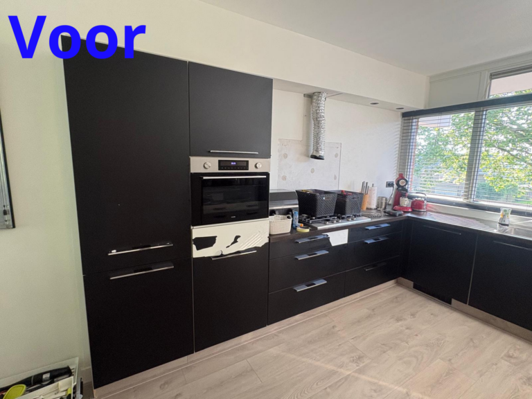 Moderne zwarte keuken met apparatuur en groot raam.