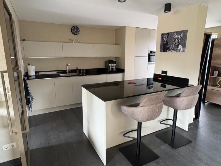 Moderne keuken met barkrukken en zwart aanrechtblad.