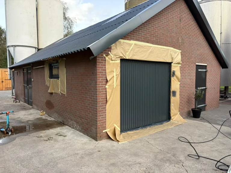 Bijgebouw in Winterswijk met afgeplakte garagedeur en kozijn tijdens het spuitwerk